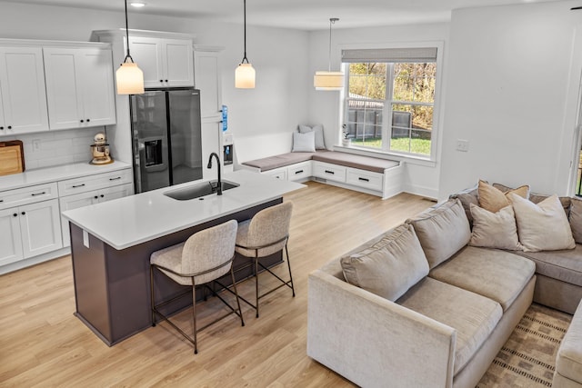 kitchen featuring pendant lighting, a kitchen bar, stainless steel refrigerator with ice dispenser, sink, and white cabinetry