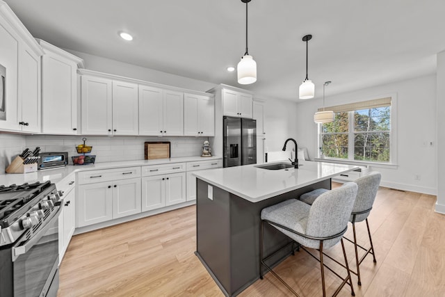 kitchen featuring a center island with sink, stainless steel appliances, hanging light fixtures, white cabinets, and sink