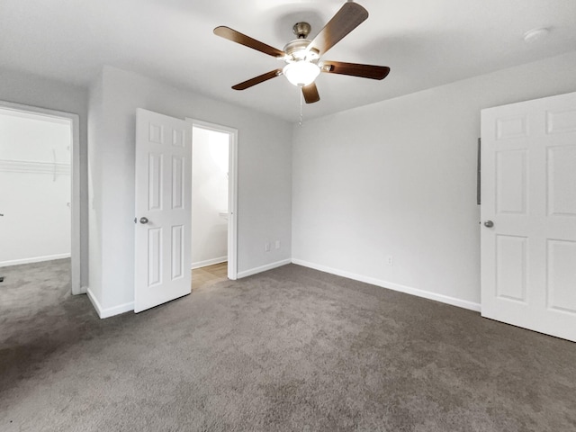 unfurnished bedroom featuring a spacious closet, connected bathroom, a closet, ceiling fan, and dark carpet