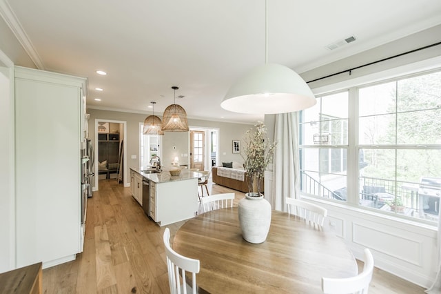 dining area with sink, ornamental molding, and light hardwood / wood-style flooring