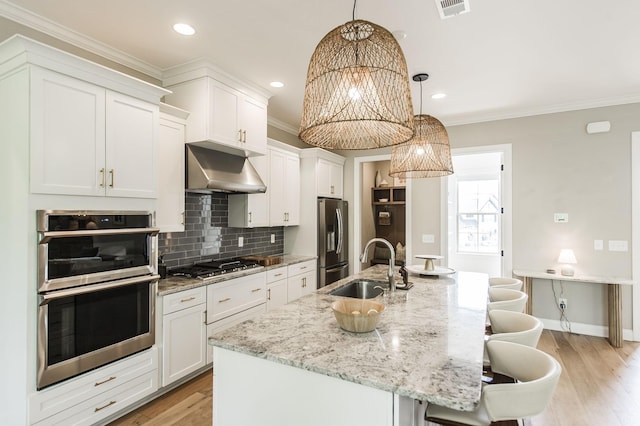 kitchen featuring appliances with stainless steel finishes, a kitchen bar, a center island with sink, and decorative light fixtures