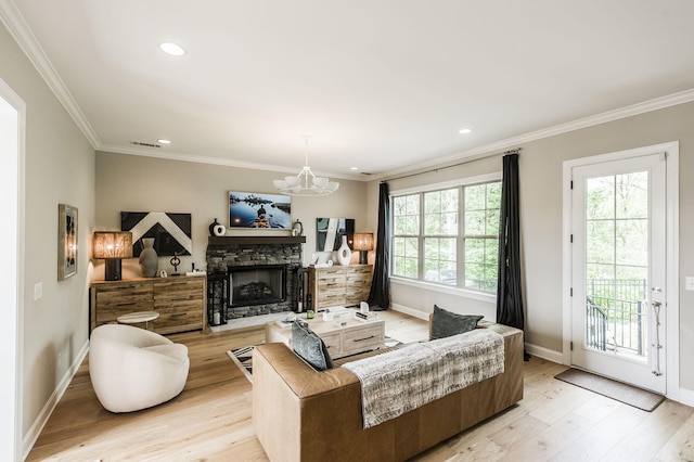 living room with light hardwood / wood-style floors, crown molding, a stone fireplace, and an inviting chandelier