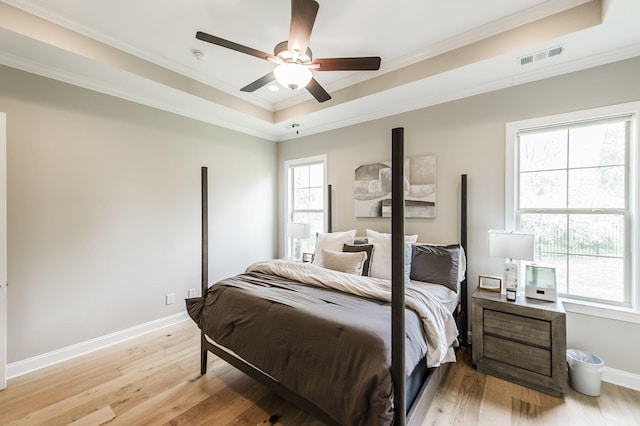 bedroom with ceiling fan, crown molding, a tray ceiling, and light hardwood / wood-style floors