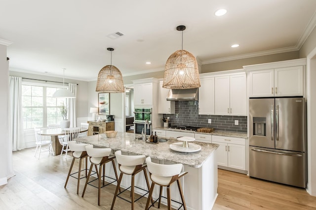 kitchen featuring light stone countertops, pendant lighting, white cabinets, appliances with stainless steel finishes, and a center island with sink