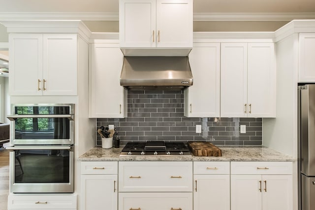 kitchen with backsplash, appliances with stainless steel finishes, wall chimney range hood, and white cabinetry