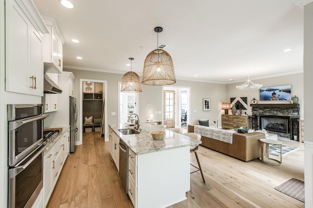 kitchen with pendant lighting, sink, an island with sink, white cabinets, and light stone counters