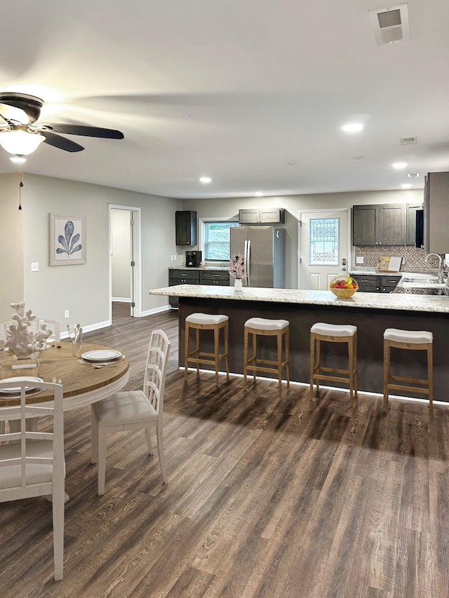 kitchen featuring dark wood-type flooring, sink, light stone counters, tasteful backsplash, and stainless steel fridge