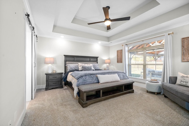 bedroom with a barn door, light carpet, ornamental molding, ceiling fan, and a tray ceiling