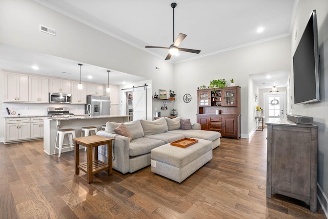 living room featuring ornamental molding, hardwood / wood-style floors, ceiling fan, and a barn door