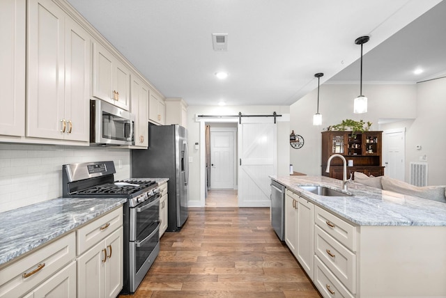 kitchen featuring a barn door, sink, decorative light fixtures, stainless steel appliances, and light stone counters