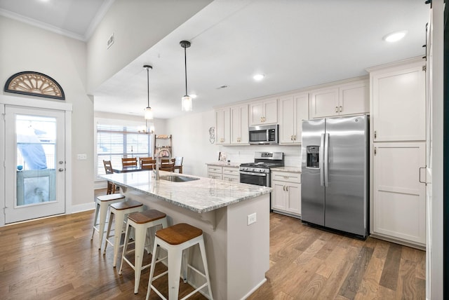 kitchen featuring white cabinets, stainless steel appliances, an island with sink, sink, and light stone counters