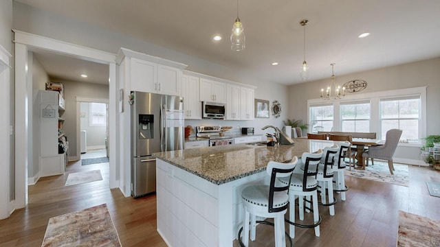 kitchen with sink, white cabinetry, hanging light fixtures, stainless steel appliances, and an island with sink