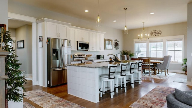 kitchen featuring sink, appliances with stainless steel finishes, white cabinetry, dark stone countertops, and a center island with sink