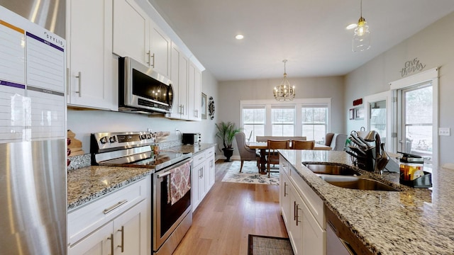 kitchen featuring sink, white cabinetry, light stone counters, hanging light fixtures, and stainless steel appliances