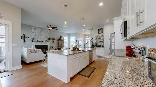 kitchen with appliances with stainless steel finishes, white cabinetry, hanging light fixtures, a kitchen island with sink, and light hardwood / wood-style floors