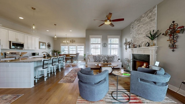 living room featuring ceiling fan with notable chandelier, light hardwood / wood-style flooring, and a large fireplace