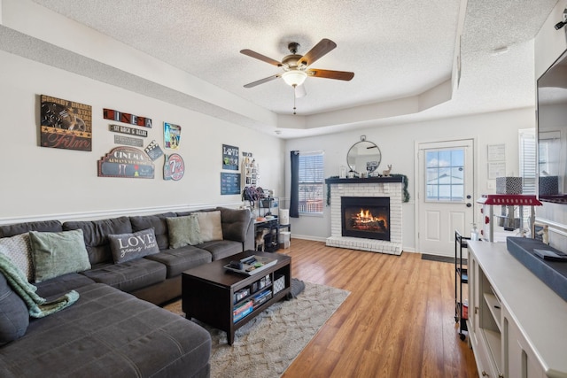 living room featuring a raised ceiling, a brick fireplace, a textured ceiling, and hardwood / wood-style flooring