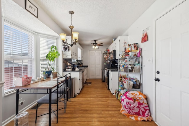 kitchen with ceiling fan with notable chandelier, a textured ceiling, white cabinets, wood-type flooring, and hanging light fixtures