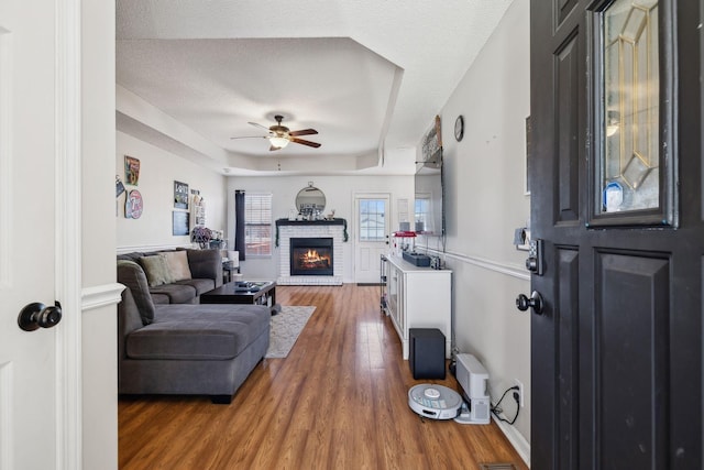 living room featuring ceiling fan, a fireplace, hardwood / wood-style floors, a tray ceiling, and a textured ceiling