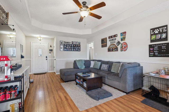 living room with a textured ceiling, ceiling fan, light hardwood / wood-style floors, and a raised ceiling