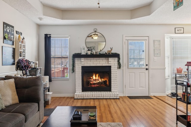 living room featuring ceiling fan, wood-type flooring, a brick fireplace, and a tray ceiling