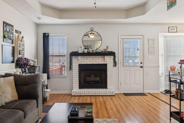 living room with a raised ceiling, ceiling fan, a brick fireplace, and hardwood / wood-style flooring