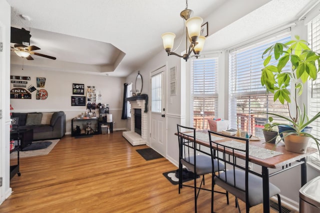 dining room featuring wood-type flooring, a tray ceiling, ceiling fan with notable chandelier, and a textured ceiling