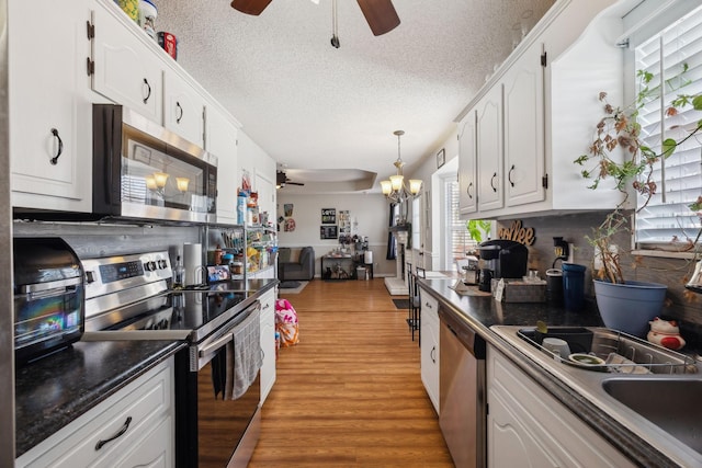 kitchen featuring appliances with stainless steel finishes, decorative light fixtures, white cabinets, light hardwood / wood-style flooring, and sink