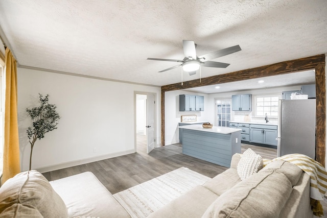 living room with sink, light hardwood / wood-style flooring, ceiling fan, ornamental molding, and a textured ceiling