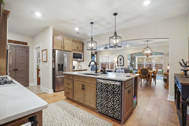 kitchen featuring pendant lighting, stainless steel appliances, light countertops, a kitchen island with sink, and a sink