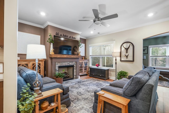 living area featuring ceiling fan, a fireplace, light wood-style floors, baseboards, and crown molding