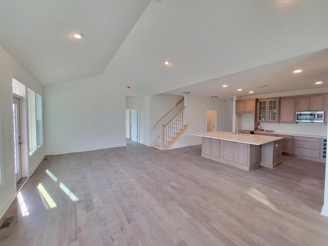 unfurnished living room with sink, lofted ceiling, and light wood-type flooring