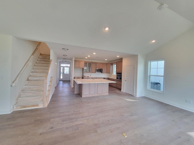 kitchen with stainless steel appliances, a kitchen island with sink, light wood-type flooring, lofted ceiling, and sink