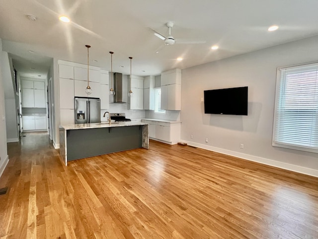 kitchen with light hardwood / wood-style floors, a center island with sink, appliances with stainless steel finishes, hanging light fixtures, and white cabinets