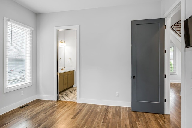 unfurnished bedroom featuring connected bathroom, wood-type flooring, and sink