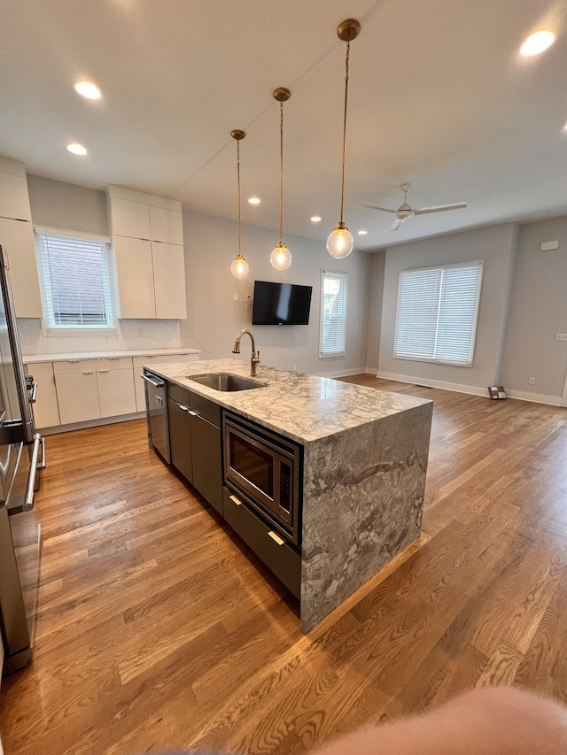 kitchen with a center island with sink, sink, white cabinetry, hanging light fixtures, and stainless steel appliances