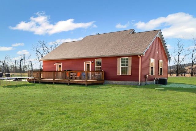 back of property featuring a wooden deck, central AC unit, a lawn, and a trampoline