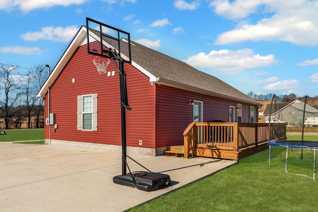 rear view of property featuring a trampoline, a deck, and a yard