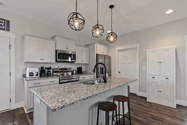 kitchen featuring decorative light fixtures, white cabinetry, stainless steel appliances, sink, and a center island with sink