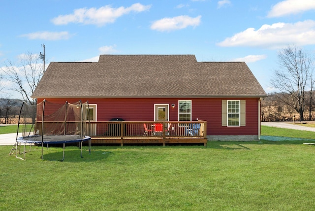 back of house featuring a deck, a lawn, and a trampoline