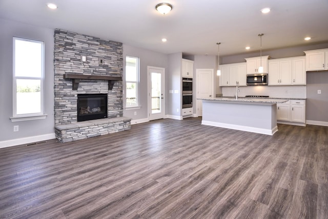 kitchen with stainless steel appliances, a kitchen island with sink, decorative light fixtures, light stone countertops, and white cabinets