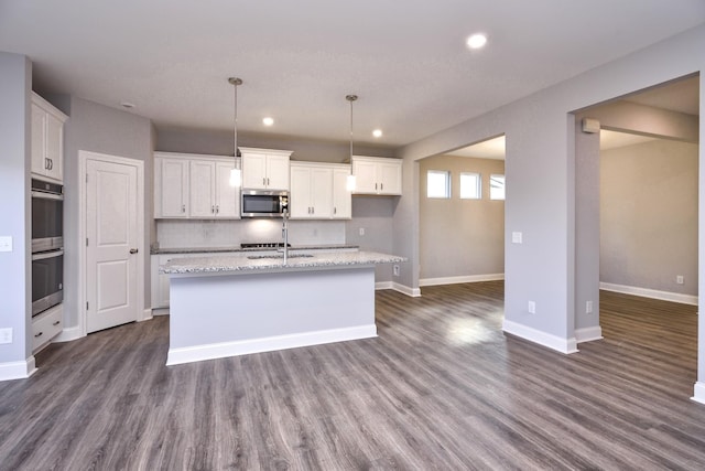 kitchen featuring white cabinetry, a center island with sink, stainless steel appliances, backsplash, and light stone countertops