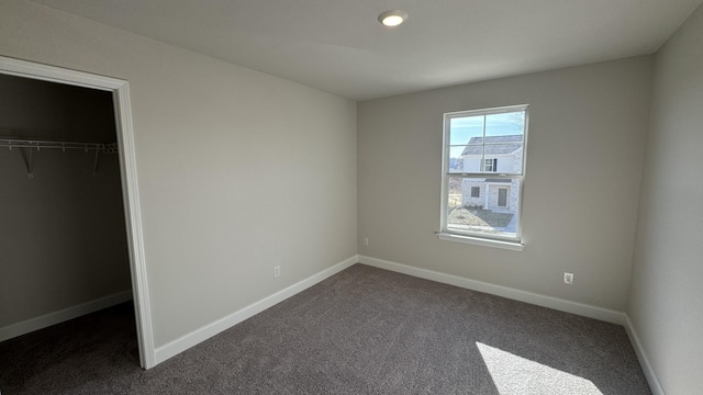 unfurnished bedroom with a spacious closet, a closet, and dark colored carpet