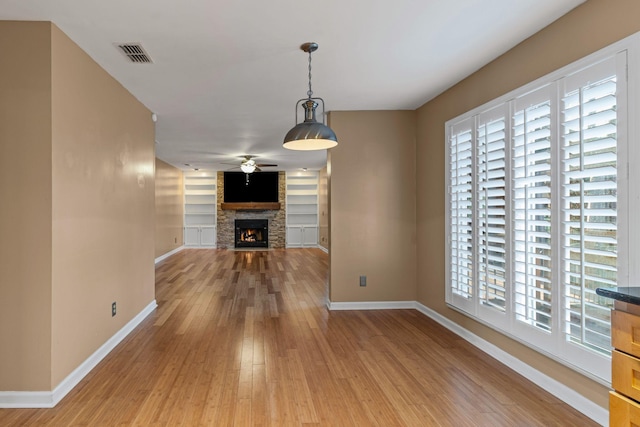 unfurnished living room with built in features, ceiling fan, hardwood / wood-style floors, and a fireplace