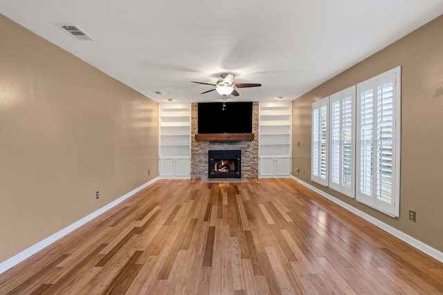 unfurnished living room with light wood-type flooring, built in shelves, ceiling fan, and a fireplace