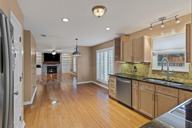 kitchen with a stone fireplace, light hardwood / wood-style floors, stainless steel dishwasher, sink, and decorative light fixtures