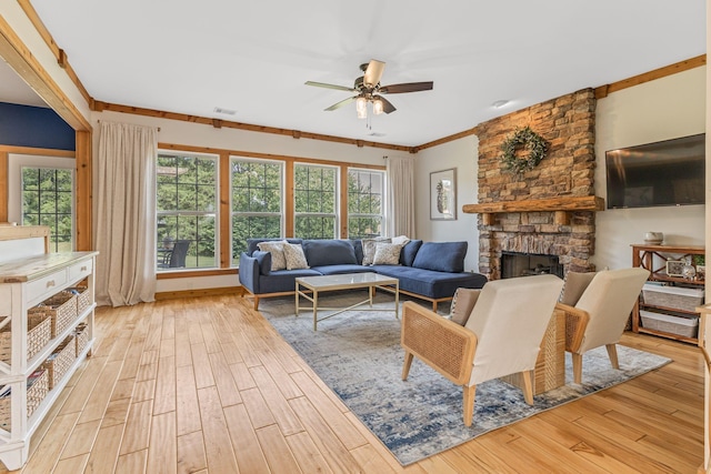 living room featuring ceiling fan, a stone fireplace, ornamental molding, and light hardwood / wood-style flooring