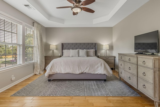 bedroom featuring light wood-type flooring, ceiling fan, and a raised ceiling