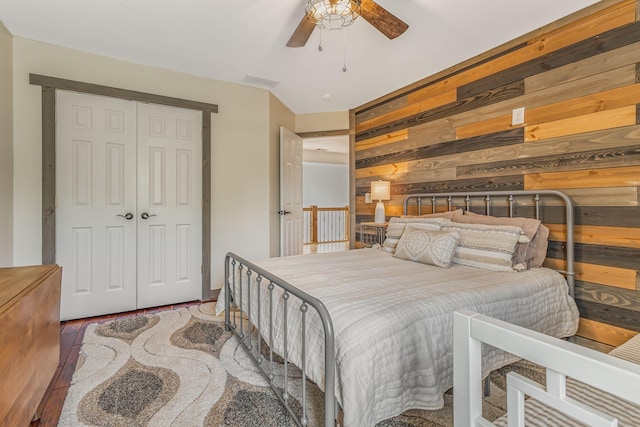 bedroom with ceiling fan, a closet, wood walls, and hardwood / wood-style floors