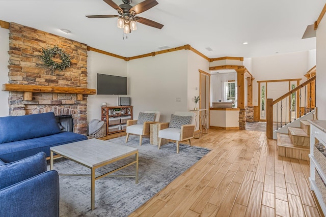 living room featuring light hardwood / wood-style floors, a large fireplace, ornamental molding, and ceiling fan